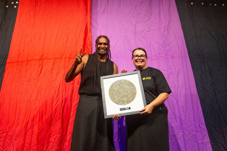Baker Boy flashing a peace sign alongside a presenter holding a framed award at the National Indigenous Music Awards (NIMAs).
